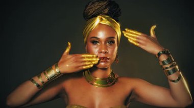 Gürültülü video. Yakın plan fantezi portresi, Afro-Amerikan kadın altın metalik makyaj gözleri, parlak dudak parlatıcısı. Altın rengi boya dansı yapan eller. Model kız. Siyah Stüdyo