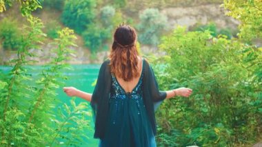 Fantezi kadın, yaz ormanı ağaç ellerinde gökyüzüne yükselmiş dua ediyor. Esrarengiz kızıl saçlı kız. Uzun, klasik mavi elbiseli, ipek kumaş. Rüzgâr gibi yavaş bir sloganla uçuyor. Seksi Kraliçe çıplak, açık bir sırt elbisesi, dikiz manzaralı. 4k.