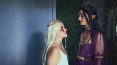 Fantezi kadın, şeytani gotik kraliçe, boğuyor, prenses sarışını cezalandırıyor, el ele tutuşuyor. Cadılar Bayramı partisi konsepti, karnaval kostümleri, elf kadın vampir sivri kulaklar, yaratıcı ortaçağ elbisesi, taç.