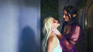 Fantezi kadın, şeytani gotik kraliçe, boğuyor, prenses sarışını cezalandırıyor, el ele tutuşuyor. Cadılar Bayramı partisi konsepti, karnaval kostümleri, elf kadın vampir sivri kulaklar, yaratıcı ortaçağ elbisesi, taç..