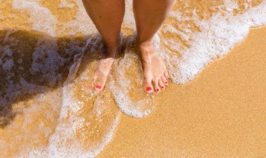 Deniz kıyısında duran genç kadının bacağında yakın çekim. Kadın bacakları 