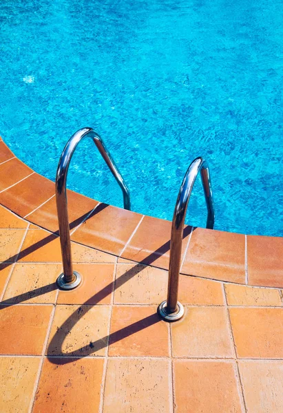 Swimming pool with stair. Grab bars ladder in the blue swimming