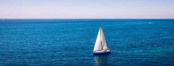 Белая парусная лодка изолирована в голубой морской воде. Парусник в море — стоковое фото