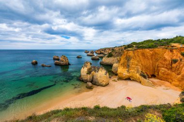 Alvor kasabası, Algarve, Portekiz 'de altın renkli taşlı çarpıcı sahil manzarası. Alvor sahilindeki kayalıkların manzarası, Algarve bölgesi, Portekiz.