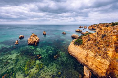 Alvor kasabası, Algarve, Portekiz 'de altın renkli taşlı çarpıcı sahil manzarası. Alvor sahilindeki kayalıkların manzarası, Algarve bölgesi, Portekiz.