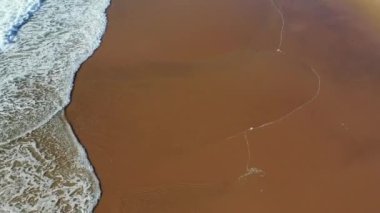 Tropik plaj hava manzarası, tropikal sarı kumsalda dalgaların üst görüntüsü. Deniz dalgaları güzel kumsalda pürüzsüz bir döngü oluşturuyor. Güzel tropik plaj havası, okyanus dalgalarının kuş bakışı görüntüsü..
