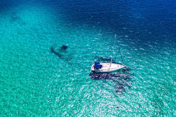 Aerial view of anchored sailing yacht in emerald sea. Aerial view of a boat. Outdoor water sports, yachting. Aerial view of anchoring yacht in open water. Ocean and sea travel and transportation