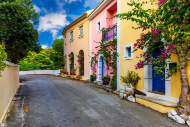 Assos, Kefalonia adasında çiçekli Yunan evleri olan geleneksel cadde. Assos köyündeki geleneksel renkli Yunan evleri. Çiçek açan fuşya çiçekleri. Kefalonia Adası, Yunanistan