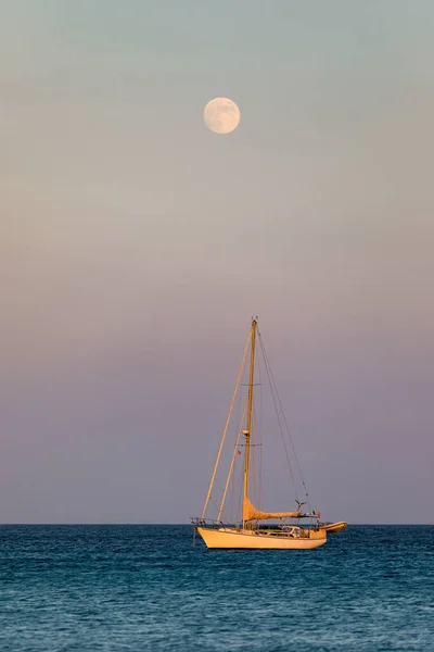 Yacht anchoring in crystal clear turquoise water in front of the tropical island, alternative lifestyle, living on a boat. Aerial view of yacht at anchor on turquoise water, showing luxury, wealth.