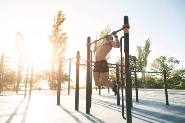Genç bir adam kendini parkta bir spor alanı yukarı çeker.
