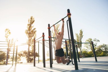 Genç bir adam kendini parkta bir spor alanı yukarı çeker.