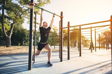 Genç bir adam kendini parkta bir spor alanı yukarı çeker.