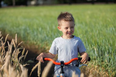 Yakışıklı bir çocuk bir buğday alanında bir bisiklet ile duruyor.