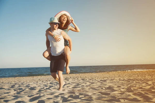 一对爱的情侣在海边玩得很开心 一个男人背着一个女人在她身后的沙子 — 图库照片