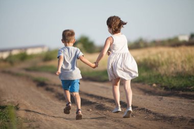 A boy and girl holding hands amicably running across the field in the summer clipart