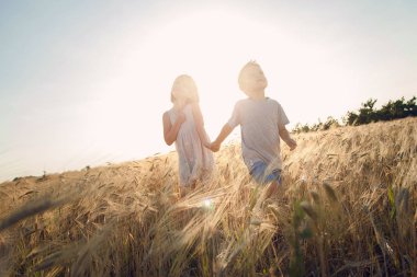 Çocuk buğday alana gitmek. Bir erkek ve bir kız elele gülmek ve eğlenmek.