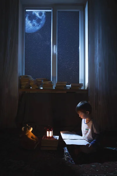 Bir kitap okumak gece ışık katta oturan bir çocuk.