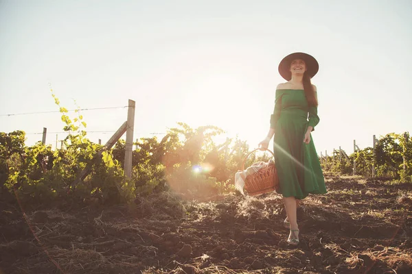 Onun elinde üzüm bağları uzun yeşil elbise ve bir sepet ile dolu bir alanda güzel bir Bayan yürür.