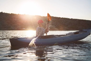 Genç bir adam bir kayık biniyor. Sessiz suları ve parlak güneş.