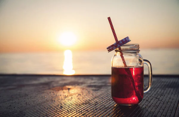 An object. A cocktail drink in a glass beaker. On open air. The sea and the sun.