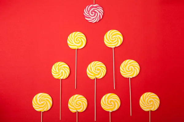 Sweet caramel candy on a red background. Bright lollipops. Yellow and pink sweets from the confectioner.