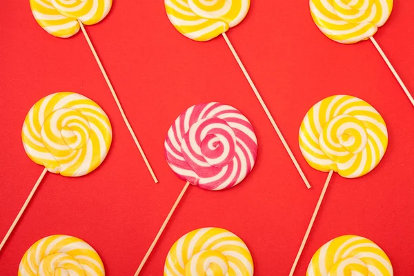 Sweet caramel candy on a red background. Bright lollipops. Yellow and pink sweets from the confectioner.