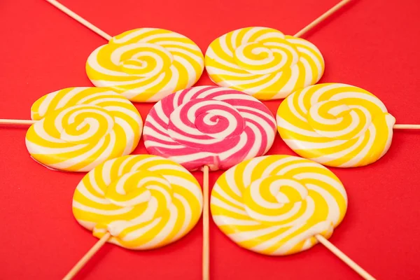 Sweet caramel candy on a red background. Bright lollipops. Yellow and pink sweets from the confectioner.