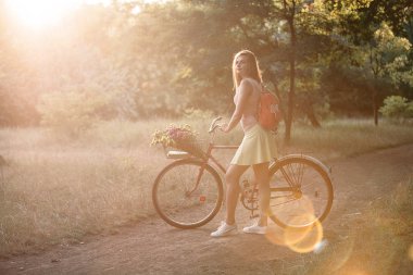 Güzel çekici kız parkta bisikletle yürüyor.