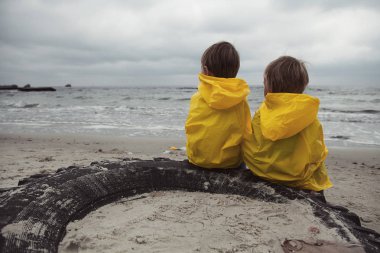          Sarı giysili iki çocuk sahilde oturup bir yana bakmak.