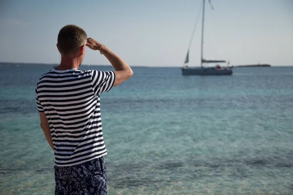 A man in sailor clothes peeking a yacht. The sailor looks into the sea.