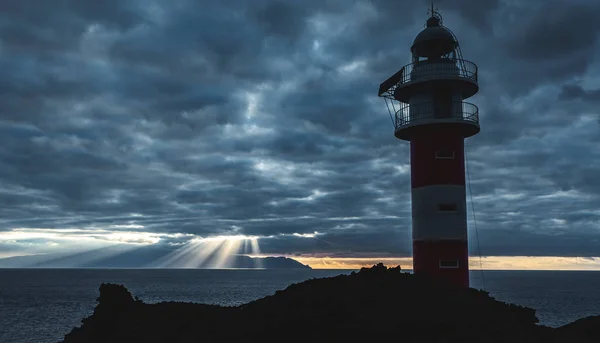 Seascape with views of the ocean, clouds, the setting sun and the lighthouse.