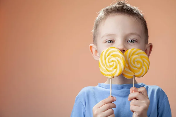 Beautiful cute boy with yellow candy on a bright background.
