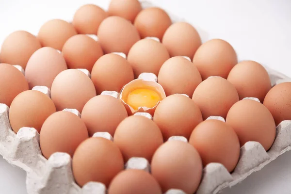 A tray of whole chicken eggs and one broken on a white background.
