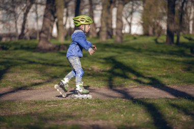 Parkta sevimli çocuk makaralar üzerinde sürmek. Güneşli ve sıcak.