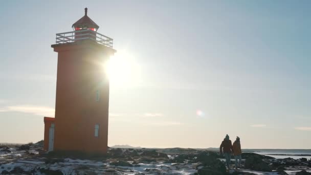 Пара, идущая рядом с маяком в Исландии — стоковое видео