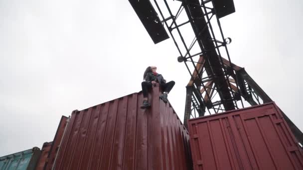 La chica se sienta en un contenedor de carga — Vídeo de stock