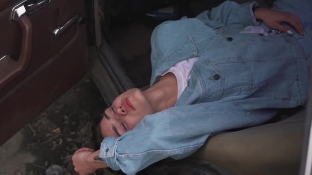 Девушка в джинсовой куртке лежит в машине — стоковое видео