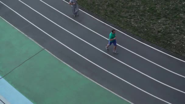 Люди бегут вдоль беговой дорожки на стадионе вид сверху — стоковое видео