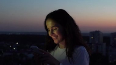 Çatıda bir akıllı telefon üzerinde günbatımında yazarak kız