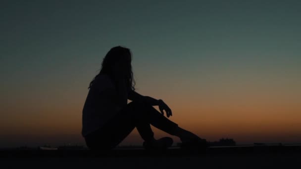 Lány ül a tetőn a naplemente — Stock videók