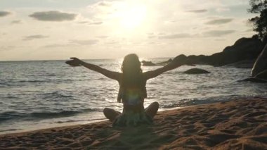 kız okyanus tarafından kum üzerinde oturan ellerini kaldırır