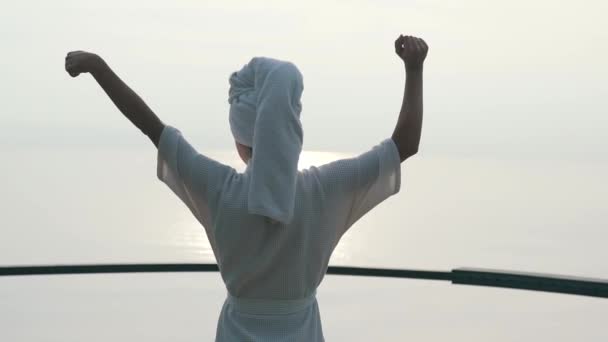 Κορίτσι με ένα μπουρνούζι υψώνει τα χέρια της το πρωί — Αρχείο Βίντεο