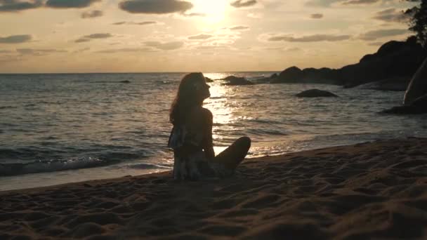 Mädchen im Urlaub sitzt am Strand bei Sonnenuntergang — Stockvideo