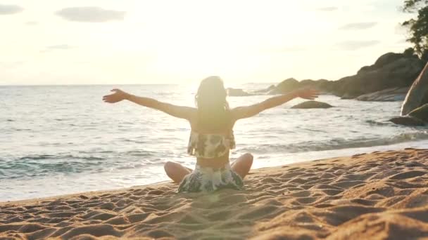 Menina levanta as mãos para cima sentado na areia junto ao oceano — Vídeo de Stock