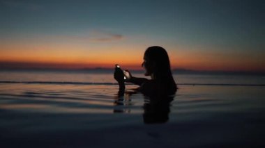 kız gün batımında havuzda akıllı telefon kullanır