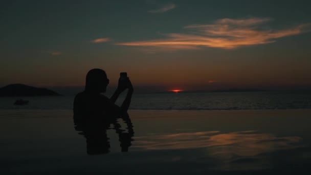 Chica fotografiando puesta de sol sentado en la piscina — Vídeos de Stock