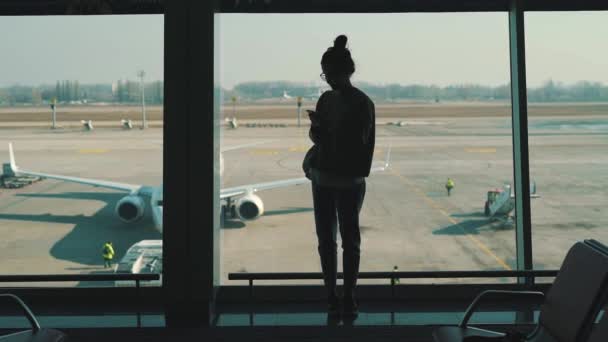 Chica de pie en la ventana en la terminal del aeropuerto — Vídeos de Stock