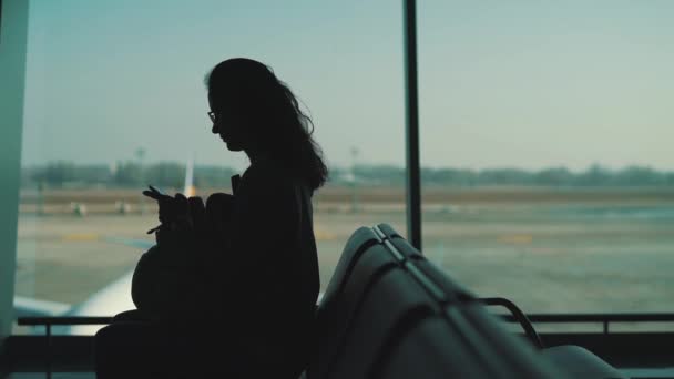 Flicka sitter vid fönstret i flygplatsterminalen — Stockvideo