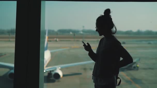 Kız havaalanı terminalinde pencerede akıllı telefon kullanır — Stok video
