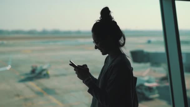 Chica utiliza teléfono inteligente en la ventana en la terminal del aeropuerto — Vídeos de Stock